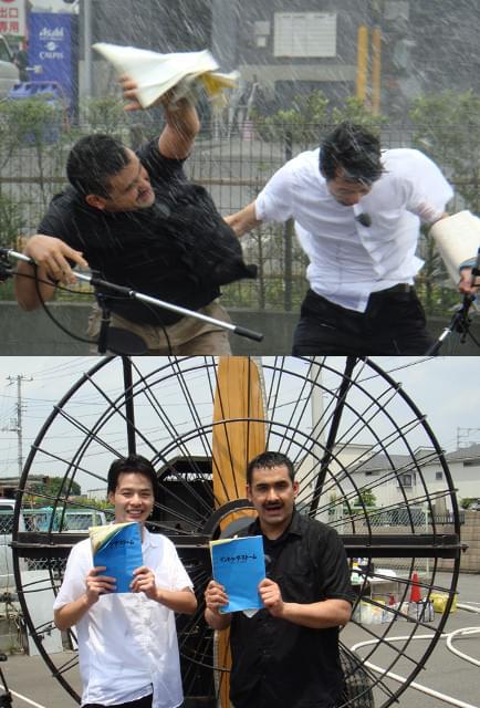 暴風雨の中で体感型アフレコに挑戦中のデニス （左から植野行雄、松下宣夫）（写真上）と 巨大扇風機を背に作品をPRする2人（写真下）