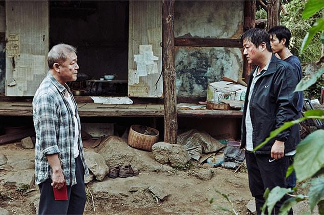 村の警官ジョング（右）は、村はずれに住む謎の日本人と対じするが……