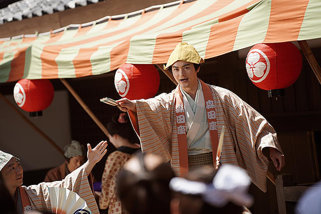 巧みな口上で客寄せとして入口に立つ木戸芸者・一八（演：瀬戸康史）